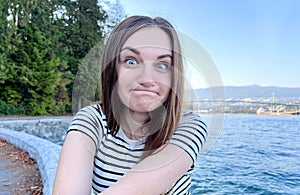 Young woman in a striped t-shirt on the background of the ocean or sea makes faces she bulged her eyes and pursed