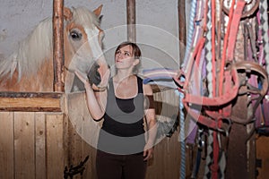Young woman stroking her horse in stable.