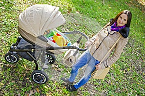 Young woman with a stroller in a city park. Happy mother with a baby stroller