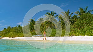Young woman strolls along the idyllic white sand beach in the sunny Maldives.