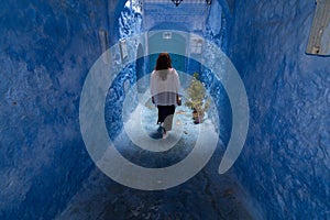 A young woman strolls through the streets of Chefchaouen, the blue town in Morocco, between the walls and the blue arches