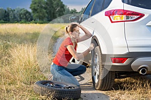 Young woman struggling to change flat car tire on countryside road