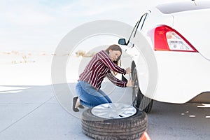 Young woman struggling to change a flat tire on the side of the highway