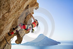 Young woman struggling to climb overhanging cliff