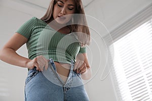 Young woman struggling to put on tight jeans at home, low angle view. Space for text