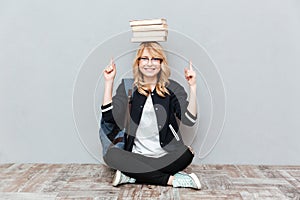 Young woman student holding books on head and pointing