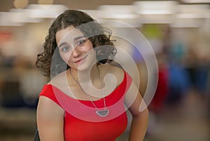 young woman student sitting in office curly hair brunette red dress in front of bokeh blur background