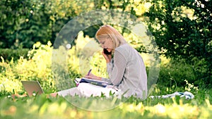 Young woman student studying while sitting in the park. Beautiful garden. Leisure activity in spring and summer.