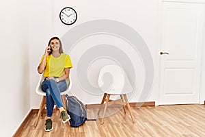 Young woman student talking on the smartphone sitting on chair at waiting room