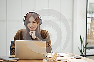 Young woman studying or working online using laptop and wearing headphones.