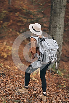 Young woman in a stylish hat and travel bag on her shoulders, looking around at the charming autumn forest