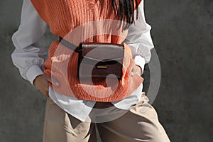 Young woman with stylish waist bag near grey wall outdoors, closeup