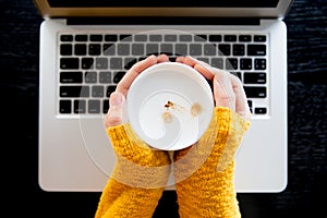 Young woman in stylish yellow sweater holding cup in hands.