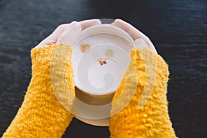 Young woman in stylish yellow sweater holding cup in hands.