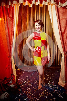 Young woman during a stylized theatrical circus photo shoot in a beautiful red location. Models posing on stage with curtain