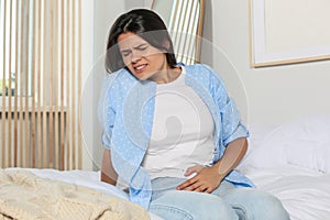 Young woman suffering from cystitis on bed at home