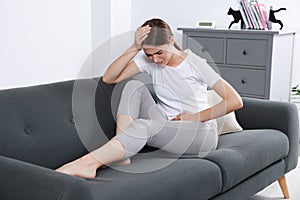 Young woman suffering from cystitis on sofa at home