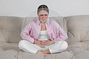 Young woman suffering from cystitis on sofa at home