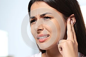Young woman suffering from ear pain on blurred background, closeup. Space for text