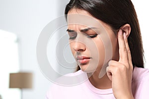 Young woman suffering from ear pain indoors, closeup. Space for text