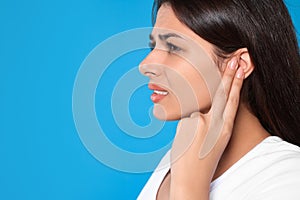 Young woman suffering from ear pain on light blue background, closeup. Space for text