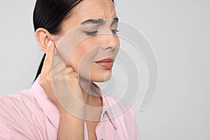 Young woman suffering from ear pain on light grey background, closeup