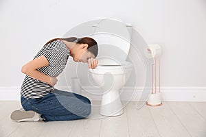 Young woman suffering from nausea at toilet bowl indoors photo