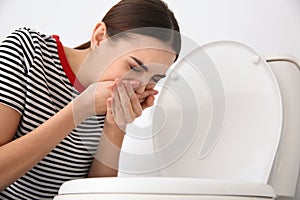 Young woman suffering from nausea at toilet bowl photo