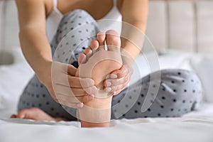 Young woman suffering from pain in foot on bed, closeup