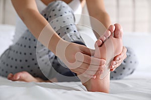 Young woman suffering from pain in foot on bed, closeup