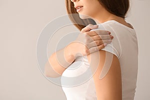 Young woman suffering from pain in shoulder on light background