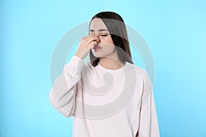 Young woman suffering from runny nose on light blue background