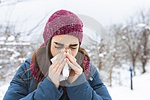 Young woman suffering from a seasonal cold and flu blowing her nose on a handkerchief as she stands outdoors on winter. Healthcare