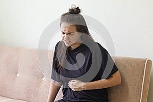 Young woman suffering from stomachache sitting at home on the sofa