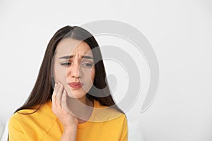 Young woman suffering from strong tooth pain on light background