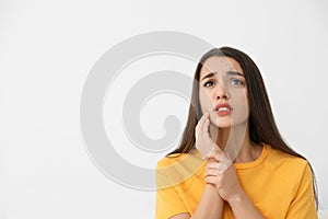 Young woman suffering from strong tooth pain on light background