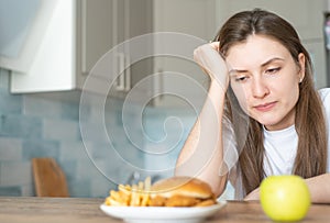 A young woman suffers because of the choice of food between harmful and healthy. The temptation to eat a hamburger with