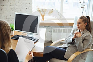 Young woman in suit sitting in office during the job interview with female employee, boss or HR-manager, talking