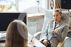 Young woman in suit sitting in office during the job interview with female employee, boss or HR-manager, talking