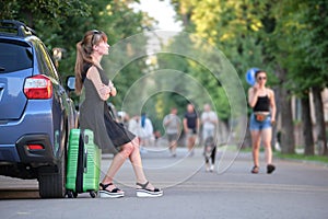 Young woman with suitcase bag waiting near her car. Travelling and vacations concept