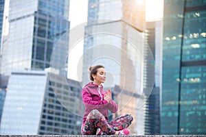 Young woman in Sukhasana pose against the skyscrapers