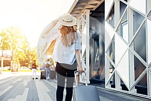 Young woman in summer clothes and hat, walks into the airport with suitcase, happy woman traveler with suitcase travel concept