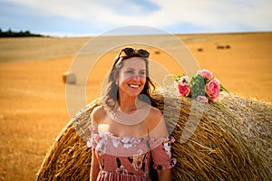 Young woman in summer dress leans against a straw bale
