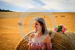 Young woman in summer dress leans against a straw bale