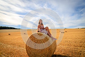 Young woman in summer dress sitting on a straw bale with flowers