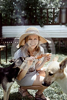 Young woman in summer hat grilling meat outdoors in the backyard, sitting with her dog
