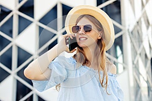 Young woman in summer hat , talking on a mobile phone at the airport, woman traveler sitting on a suitcase, near the airport