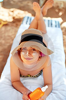 Young woman with sun cream on face holding sunscren bottle on the beach.