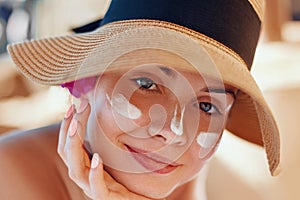 Young woman with sun cream on face holding sunscren bottle on the beach.