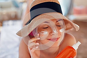 Young woman with sun cream on face holding sunscren bottle on the beach.